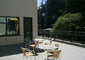 an angled view of a balcony patio with tables and chairs. A wall encloses the patio with a door